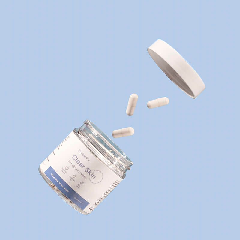 Skinbiotics embalaža z odprtim pokrovom, modra podlaga, in nje letijo kapsule