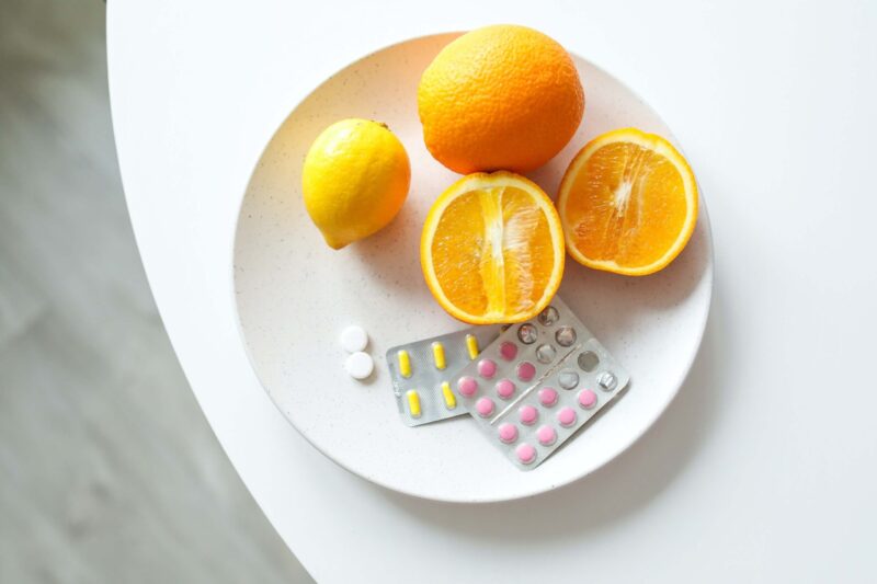 Prerezana in cela pomaranča na belem krožniku na mizi, zravn so raznorazna zdravila