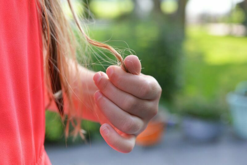Ženska se drži za konice las s svojimi prsti, v ozadju zelenje